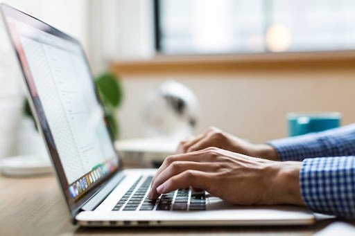 Individual typing on a laptop, representing the importance of knowledge sharing in utility risk mitigation and compliance.